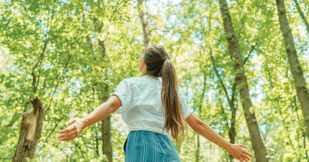 Teen facing away, looking up at a brightly lit forest.